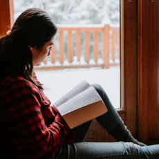 Een vrouw zit voor het raam en leest in haar eentje de Bijbel