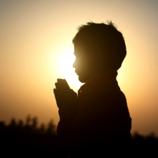 A man praying in front of a rising sun